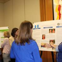 A group of attendees standing around another poster presentation, asking questions